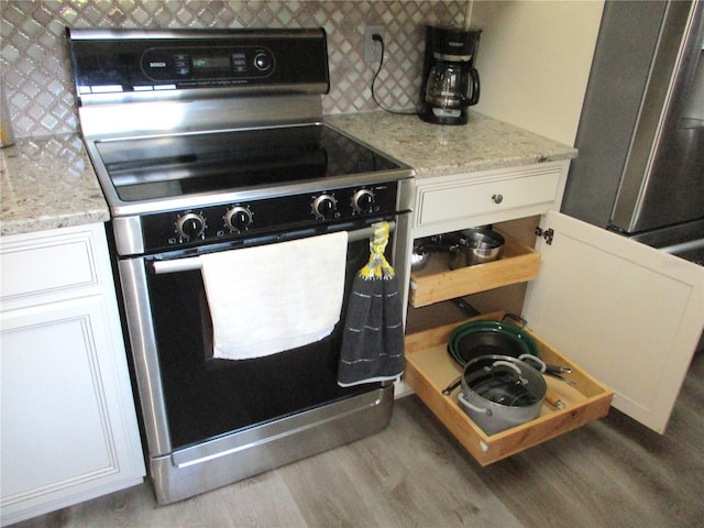 kitchen with stainless steel electric stove, white cabinets, light stone counters, and wood finished floors