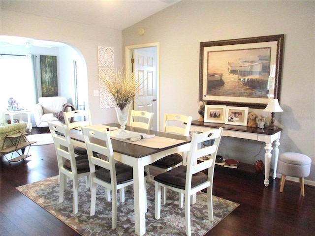 dining area featuring dark wood-type flooring, arched walkways, and vaulted ceiling