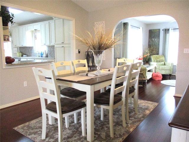 dining room featuring baseboards, arched walkways, and dark wood-style flooring