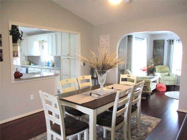 dining room with dark wood-type flooring, arched walkways, and lofted ceiling