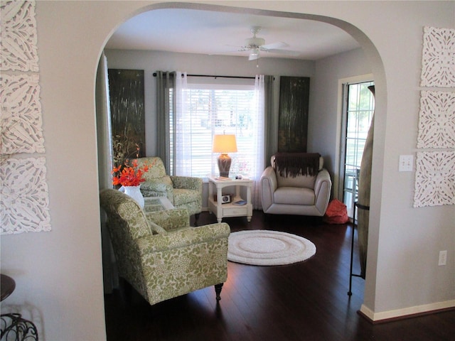 living room featuring arched walkways, dark wood-type flooring, a ceiling fan, and baseboards