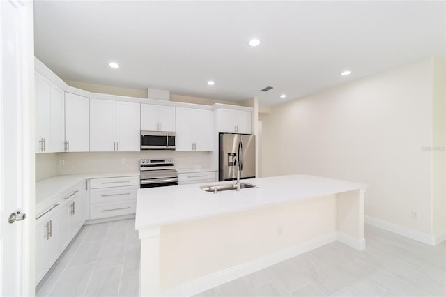 kitchen with sink, stainless steel appliances, white cabinets, and a center island with sink