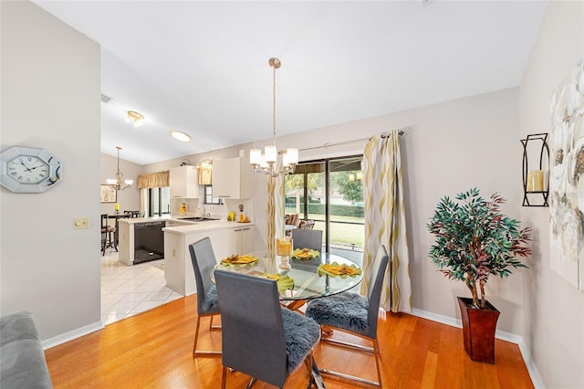 dining room with lofted ceiling, sink, light hardwood / wood-style flooring, and a notable chandelier