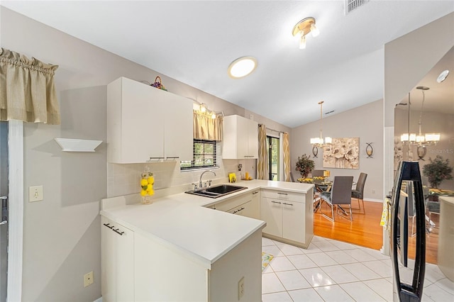 kitchen featuring vaulted ceiling, sink, white cabinets, kitchen peninsula, and an inviting chandelier