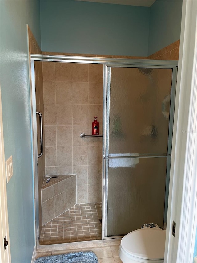 bathroom with tile patterned flooring, a shower with shower door, and toilet