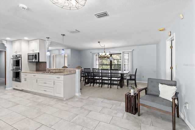 kitchen with stainless steel appliances, pendant lighting, white cabinets, and light stone counters