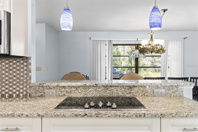 kitchen featuring black electric stovetop, hanging light fixtures, and white cabinets