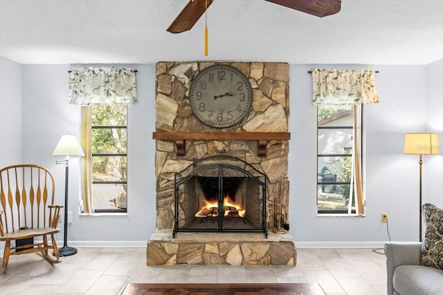 living area with ceiling fan, a stone fireplace, and a textured ceiling