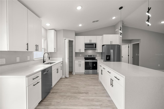 kitchen with pendant lighting, sink, appliances with stainless steel finishes, white cabinetry, and vaulted ceiling