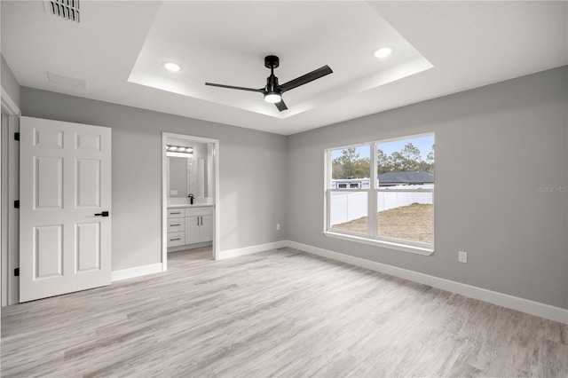 unfurnished bedroom featuring connected bathroom, a tray ceiling, light hardwood / wood-style flooring, and ceiling fan