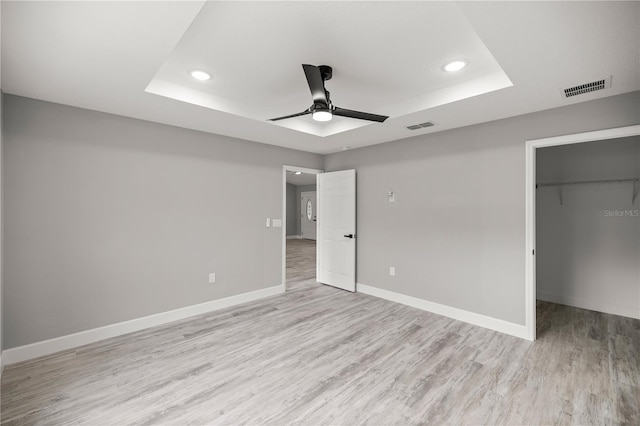 unfurnished bedroom featuring a closet, a spacious closet, ceiling fan, and a tray ceiling