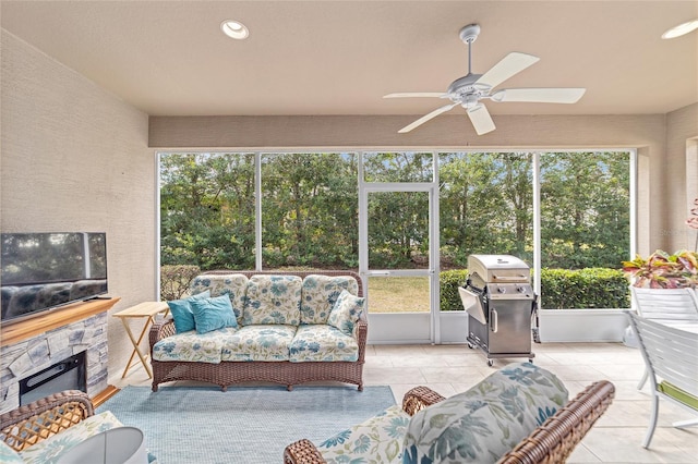 sunroom / solarium featuring a stone fireplace and ceiling fan