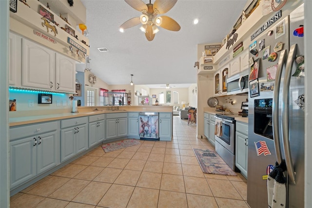 kitchen with light tile patterned flooring, sink, hanging light fixtures, kitchen peninsula, and stainless steel appliances