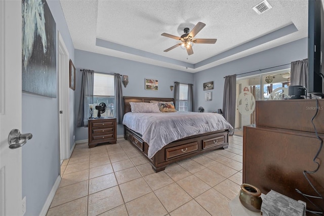 tiled bedroom featuring ceiling fan, a textured ceiling, and a tray ceiling