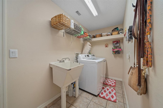 washroom with light tile patterned flooring, sink, washing machine and clothes dryer, and a textured ceiling