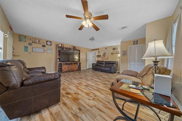 living room featuring ceiling fan, a textured ceiling, and light wood-type flooring