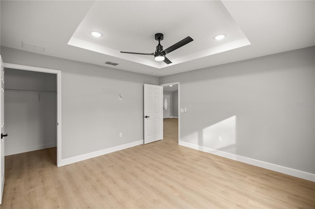 unfurnished bedroom with ceiling fan, a tray ceiling, light hardwood / wood-style floors, and a spacious closet