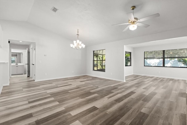 empty room featuring ceiling fan with notable chandelier, light hardwood / wood-style floors, and vaulted ceiling