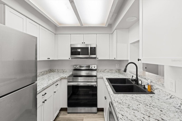 kitchen featuring sink, light hardwood / wood-style flooring, stainless steel appliances, light stone countertops, and white cabinets