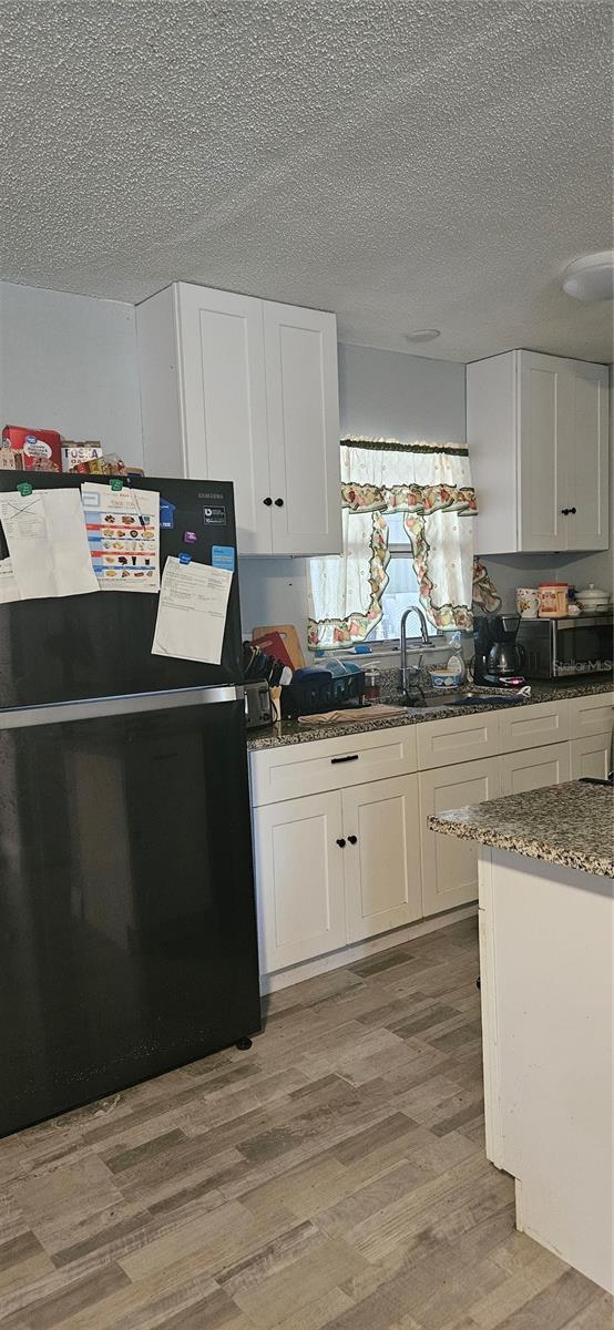 kitchen with white cabinetry, sink, light wood-type flooring, and black fridge