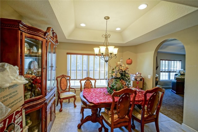 dining area featuring a tray ceiling, light tile patterned floors, and a notable chandelier