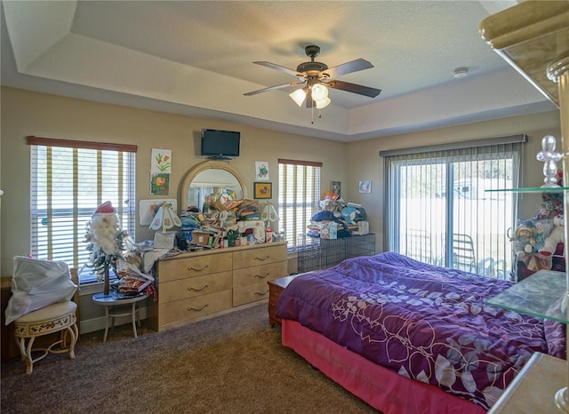 carpeted bedroom with multiple windows, ceiling fan, and a tray ceiling