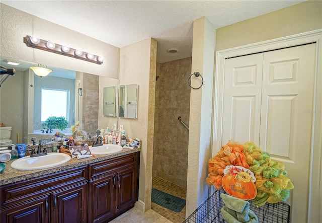 bathroom with a tile shower, vanity, toilet, tile patterned floors, and a textured ceiling