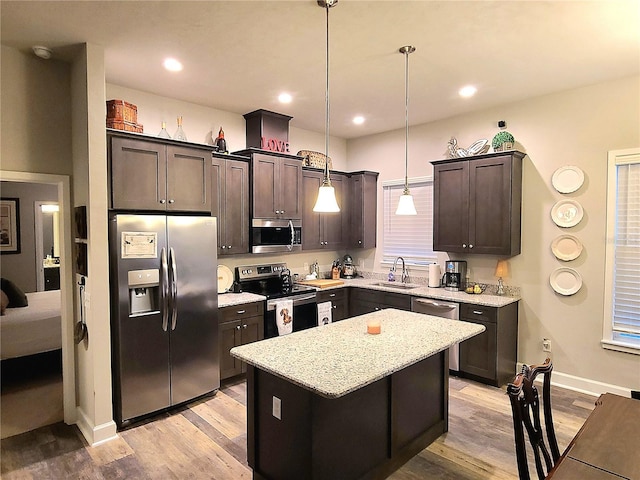 kitchen with appliances with stainless steel finishes, pendant lighting, sink, a center island, and light wood-type flooring