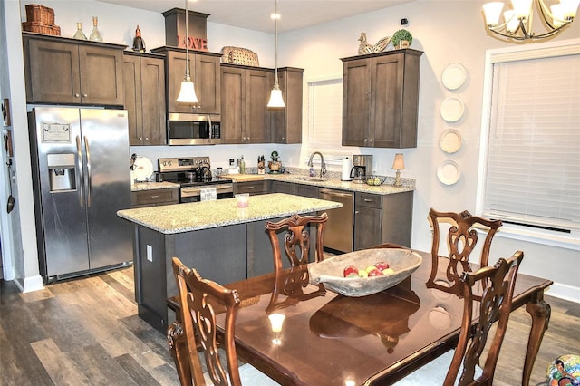 kitchen featuring sink, light stone counters, hanging light fixtures, appliances with stainless steel finishes, and a kitchen island