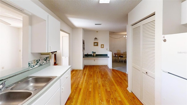 kitchen featuring sink, light hardwood / wood-style floors, a textured ceiling, and white cabinets