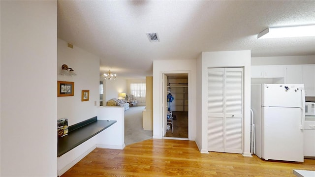 kitchen with a textured ceiling, light wood-type flooring, white fridge, a notable chandelier, and white cabinets