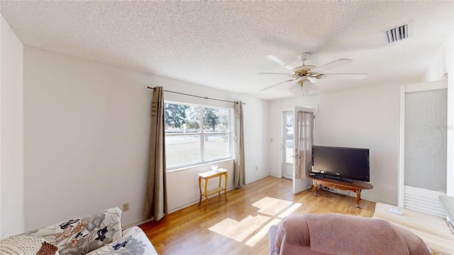 living room with ceiling fan, light hardwood / wood-style floors, and a textured ceiling