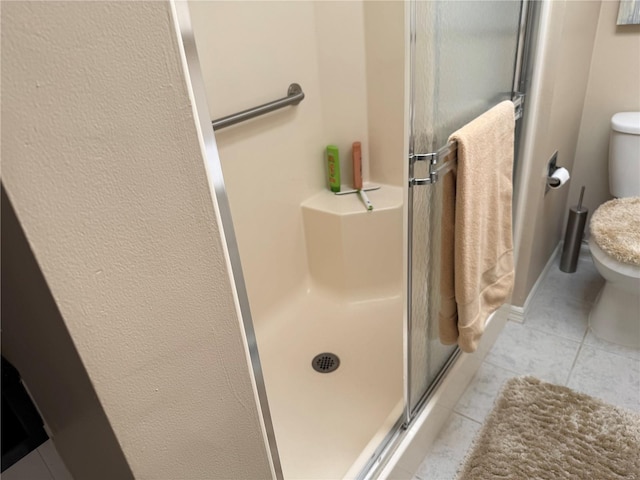 bathroom featuring tile patterned floors, toilet, and a shower with shower door