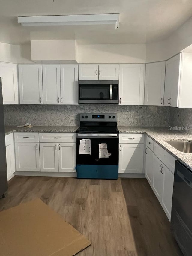 kitchen featuring sink, white cabinetry, hardwood / wood-style floors, stainless steel appliances, and tasteful backsplash