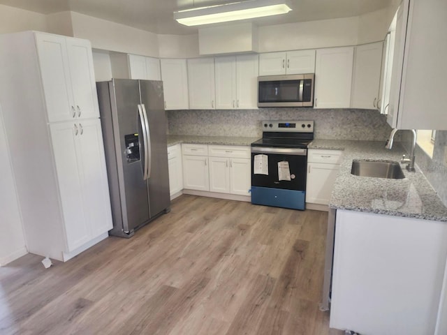 kitchen with sink, appliances with stainless steel finishes, white cabinetry, tasteful backsplash, and light stone countertops