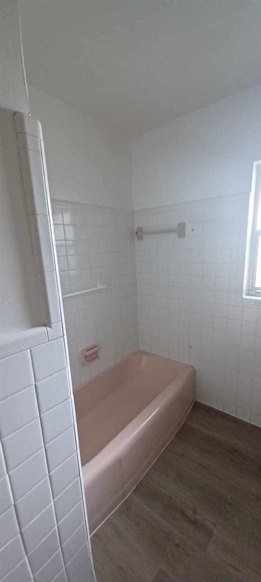 bathroom featuring hardwood / wood-style flooring,  shower combination, and tile walls