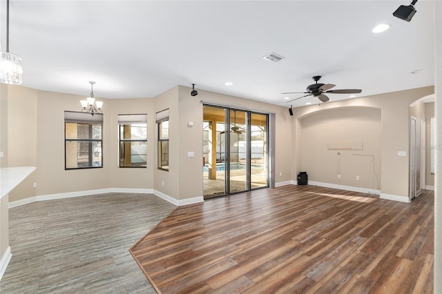 unfurnished living room with ceiling fan with notable chandelier and dark wood-type flooring