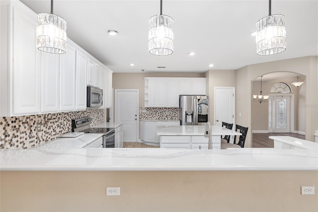 kitchen featuring stainless steel appliances, white cabinets, pendant lighting, and a notable chandelier