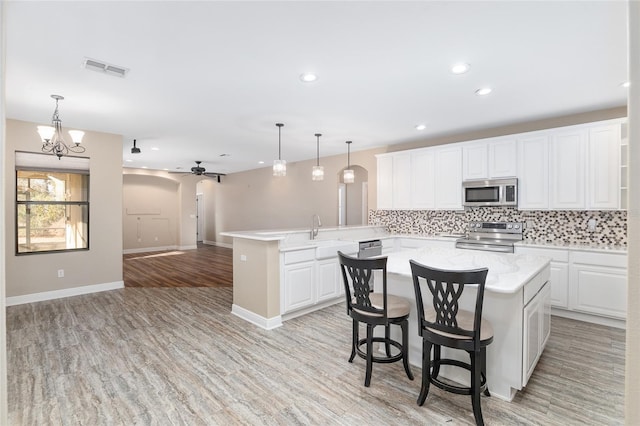 kitchen featuring a kitchen island, appliances with stainless steel finishes, white cabinets, hanging light fixtures, and kitchen peninsula