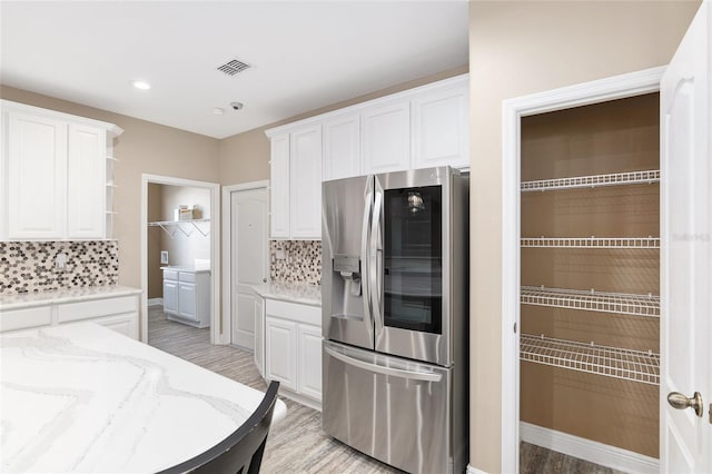 kitchen featuring decorative backsplash, light hardwood / wood-style floors, stainless steel refrigerator, and white cabinets