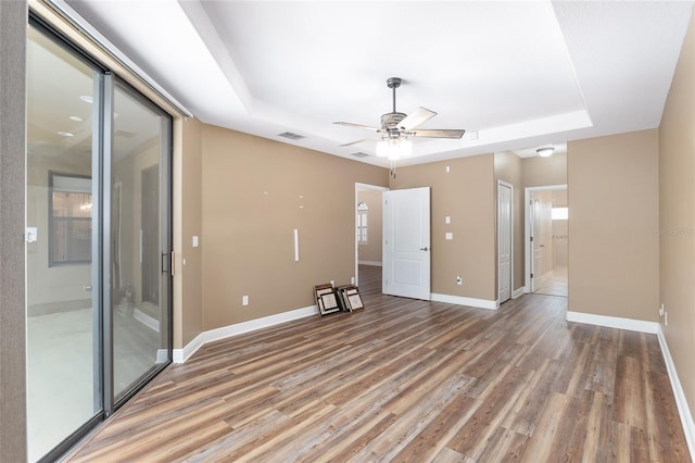 empty room with hardwood / wood-style floors, a raised ceiling, and ceiling fan