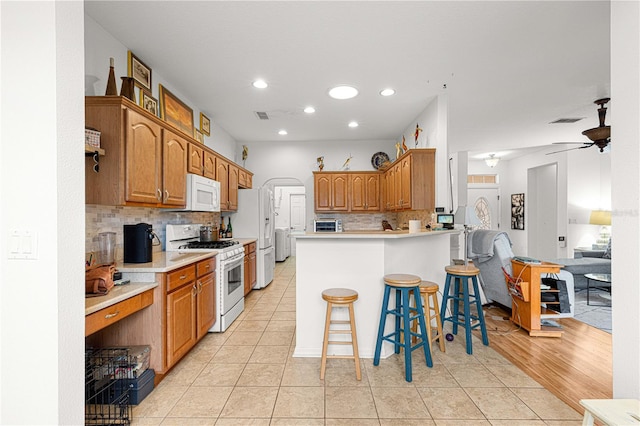 kitchen with light tile patterned flooring, a kitchen bar, backsplash, and white appliances