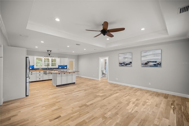 interior space with white cabinetry, stainless steel fridge, a tray ceiling, and a kitchen island