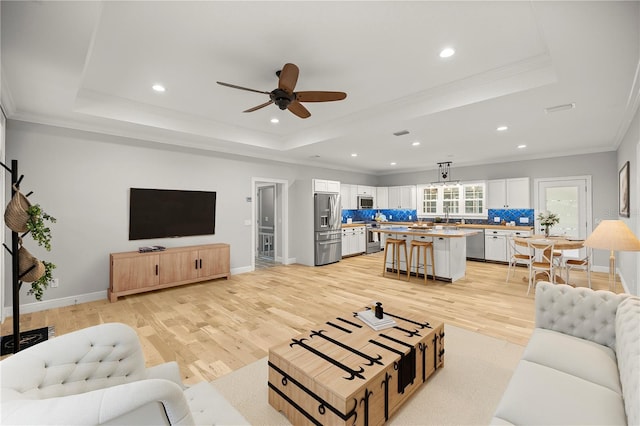 living room with sink, crown molding, light hardwood / wood-style floors, and a raised ceiling