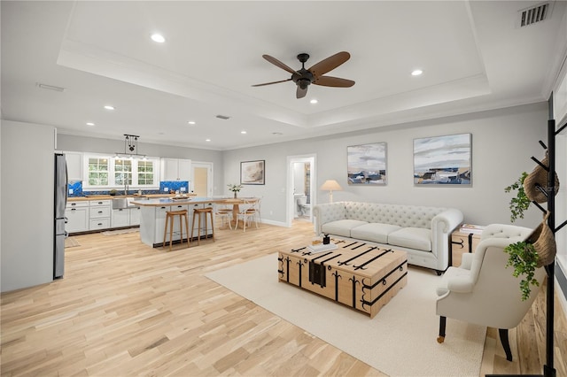 living room featuring ornamental molding, light wood-type flooring, and a tray ceiling