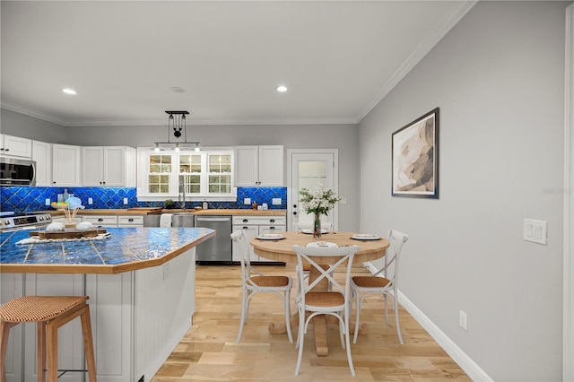 kitchen featuring stainless steel appliances, white cabinetry, a breakfast bar, and decorative light fixtures