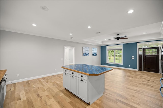 kitchen featuring crown molding, light wood-type flooring, a raised ceiling, a kitchen island, and white cabinets