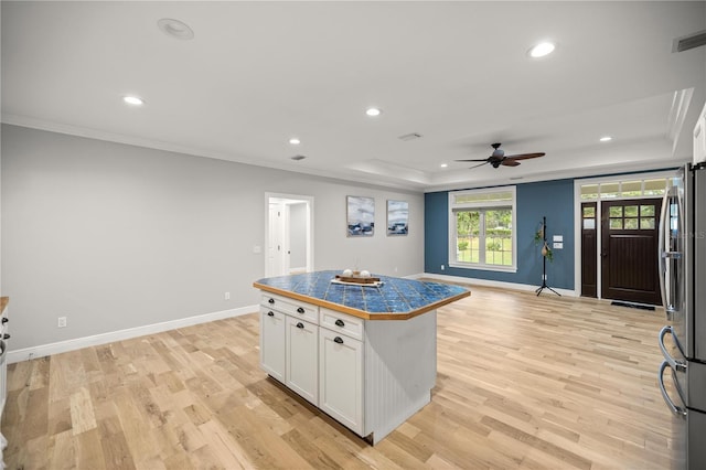 kitchen with crown molding, white cabinetry, a center island, a raised ceiling, and light wood-type flooring