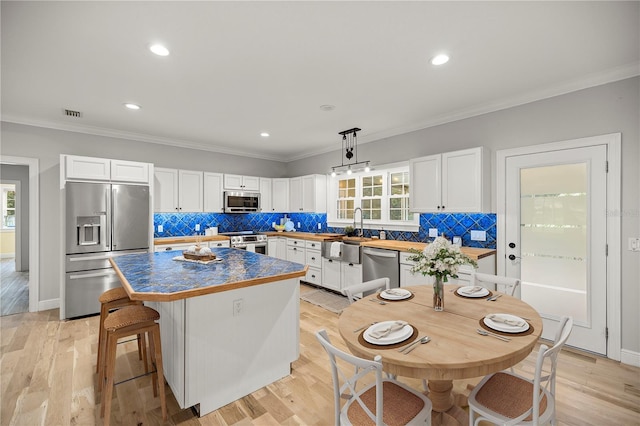 kitchen featuring pendant lighting, light hardwood / wood-style flooring, appliances with stainless steel finishes, a center island, and white cabinets