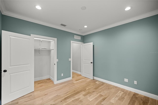 unfurnished bedroom featuring crown molding, a walk in closet, light hardwood / wood-style floors, and a closet